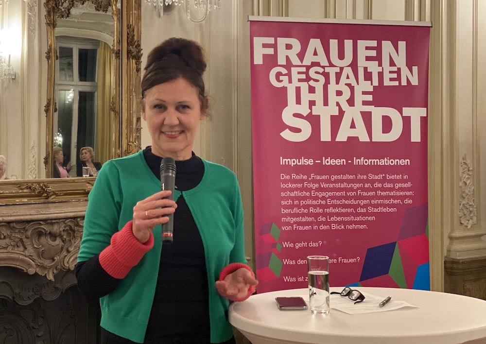 Das Foto zeigt die Kommunalpolitikerin Claudia Wiese vor einem Plakat mit der "Aufschrift Frauen gestalten ihre Stadt"